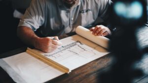 man sitting at desk drawing a building plan
